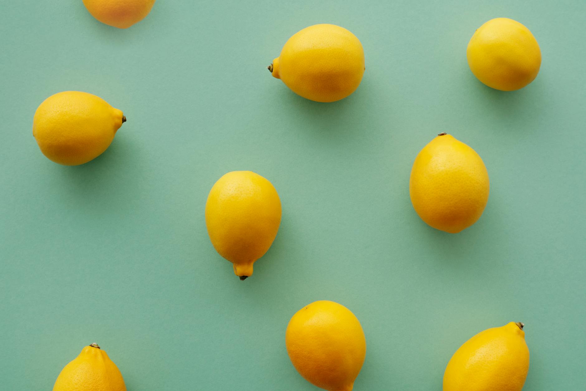 Limoni gialli vivaci disposti su uno sfondo verde pastello, che creano una composizione piatta fresca e vibrante