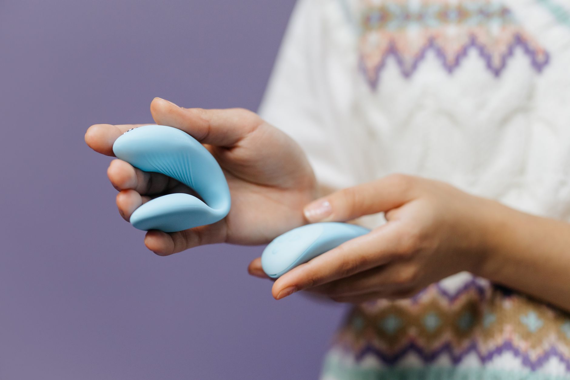 Mani che tengono un vibratore blu elegante contro uno sfondo viola, simboleggiando sensibilità e intimità