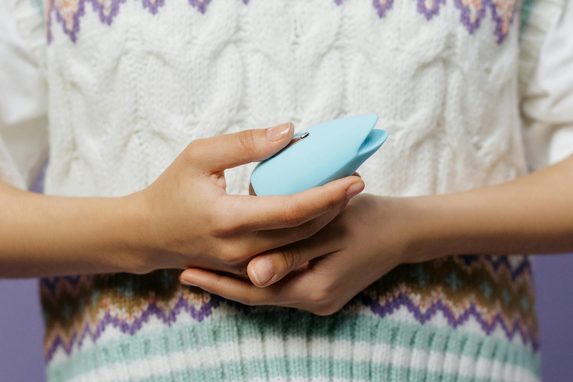 Due mani che tengono vibratori in silicone rosa e blu su uno sfondo pastello.